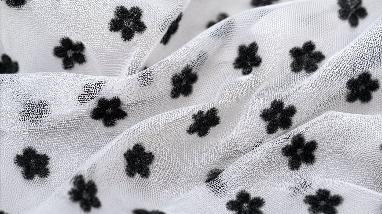 Tule branco flocado com pequenas flores pretas distribuídas sobre a malha
