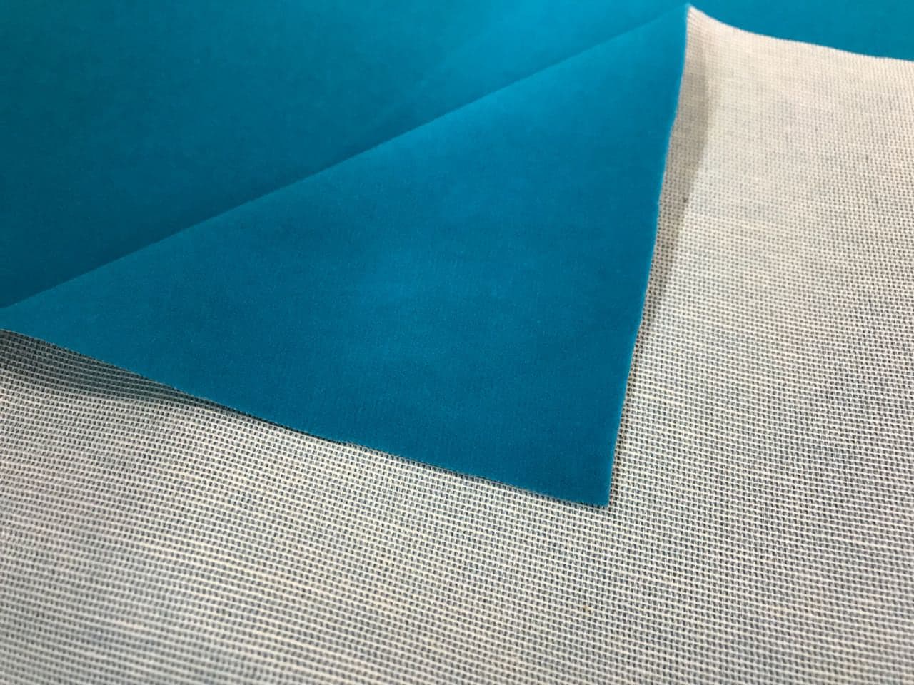 Veludo azul-turquesa com a ponta dobrada, mostrando o verso de tecido cru de trama aberta