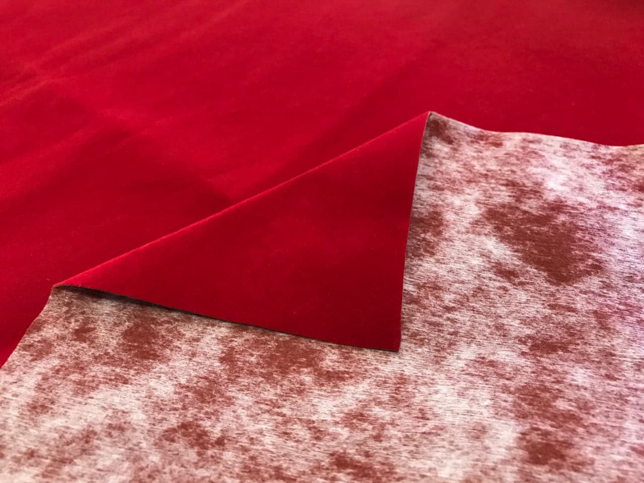 Veludo vermelho com a ponta dobrada, mostrando o verso de manta de poliéster com manchas rosadas